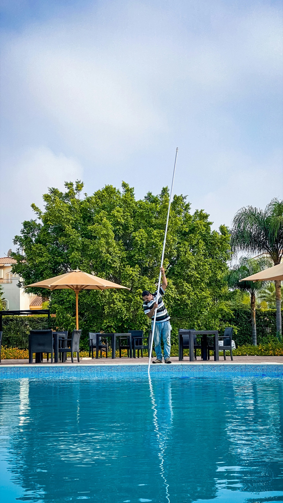 Pool technician cleaning a large pool with a long pole.